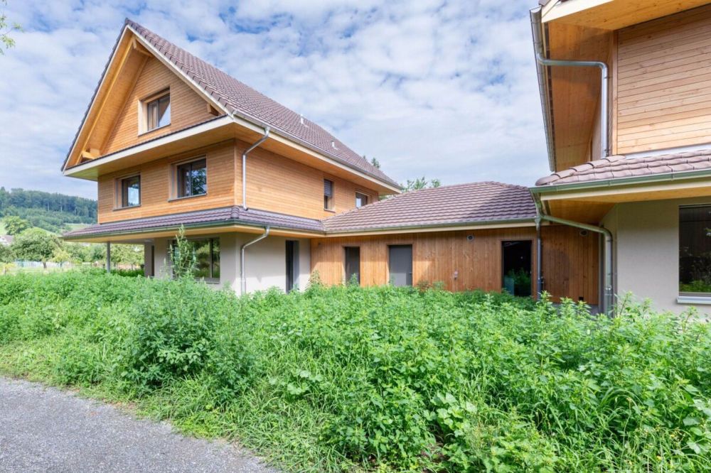 Nachhaltiges Wohnerlebnis aus Holz - Hausansicht mit Carport und Nachbarshaus