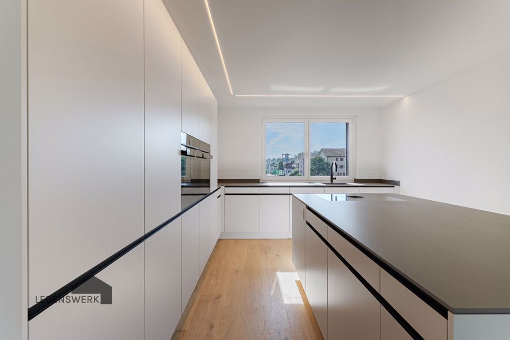 Modern Living - Licht und Lebensfreude am Wiibärg, Kreuzlingen TG - OF - Die elegante Deckenlinien-Beleuchtung setzt die Kochinsel stilvoll in Szene und sorgt für stimmungsvolles Licht