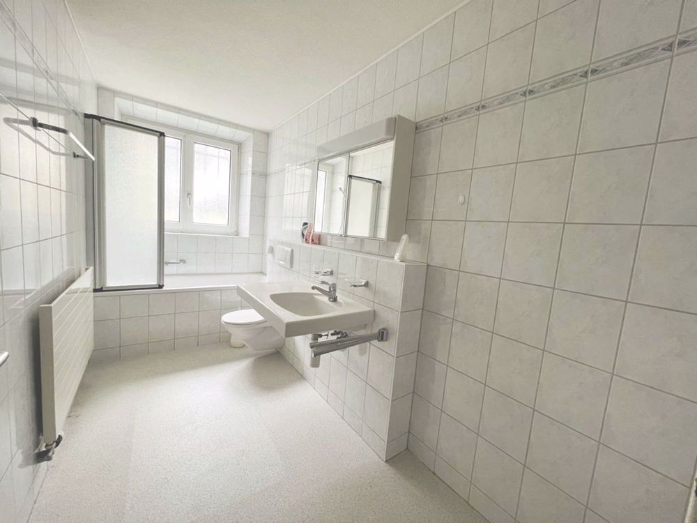 Badezimmer mit Tageslicht, Badewanne, Toilette und Lavabo mit Spiegelschrank (der Boden wird mit weissen Platten verlegt)