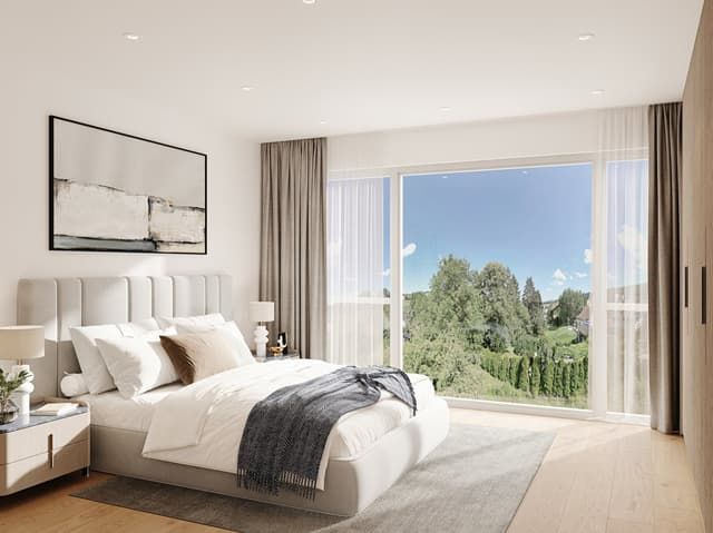 Magnifique maison individuelle à Courfaivre JU - Spacious bedroom with large windows offering a scenic view of the surrounding trees and landscape. The room features a plush white bed with decorative pillows, a modern artwork on the wall, and neutra