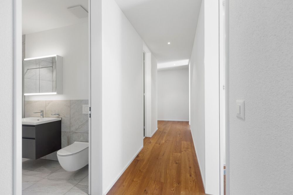 Einziehen und geniessen: Neue 4.5-Zimmer-Wohnung im Ziegelei-Quartier - Einladender Korridor mit durchgehendem Echtholzparkett und Blick ins stilvolle Bad.