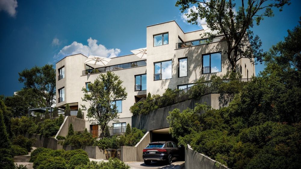 Neubau Attika-Maisonette am Heidenweg - Multi-story apartment building with balconies, surrounded by trees and greenery, with a parking area in the foreground